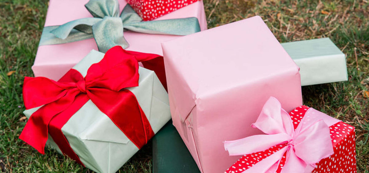 Several wrapped gift boxes in pink, red, and light green paper with large satin bows, announcing PRODOH's 2026 Holiday collection