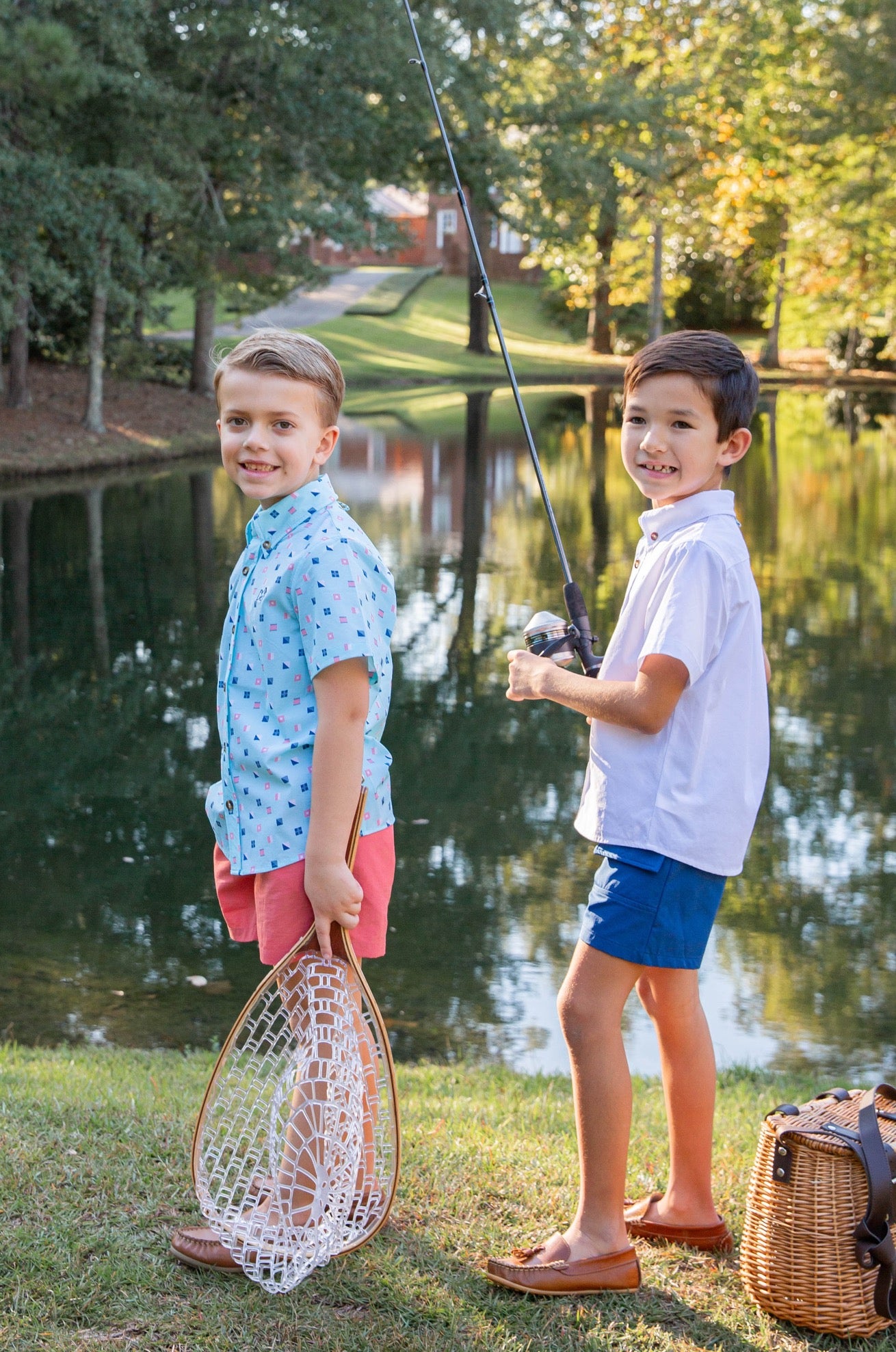 Two children by a lake, one holding a fishing net and the other a fishing rod.