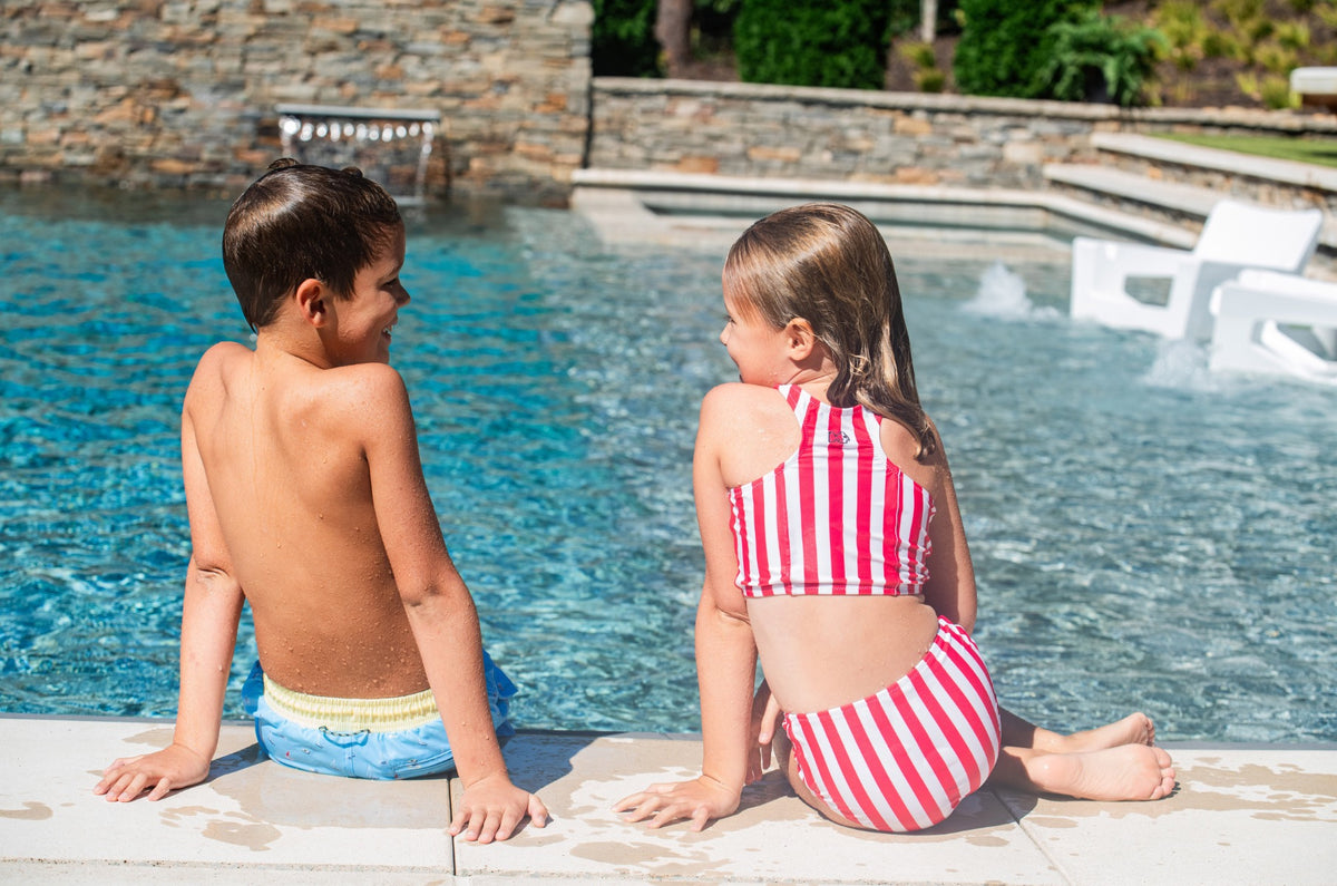 Two children sitting by a poolside wearing with girl wearing Red Stripe bikini