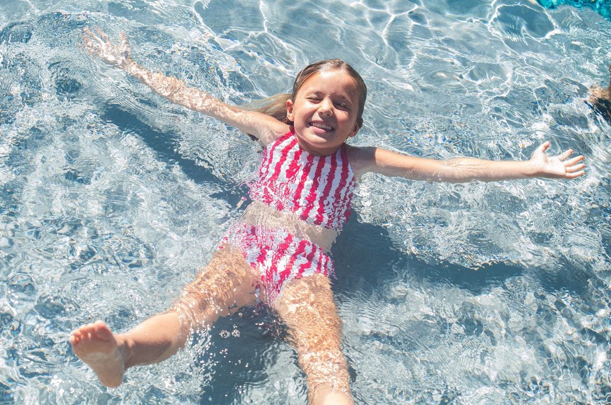 Child in a red and white striped swimsuit floating in clear blue water.
