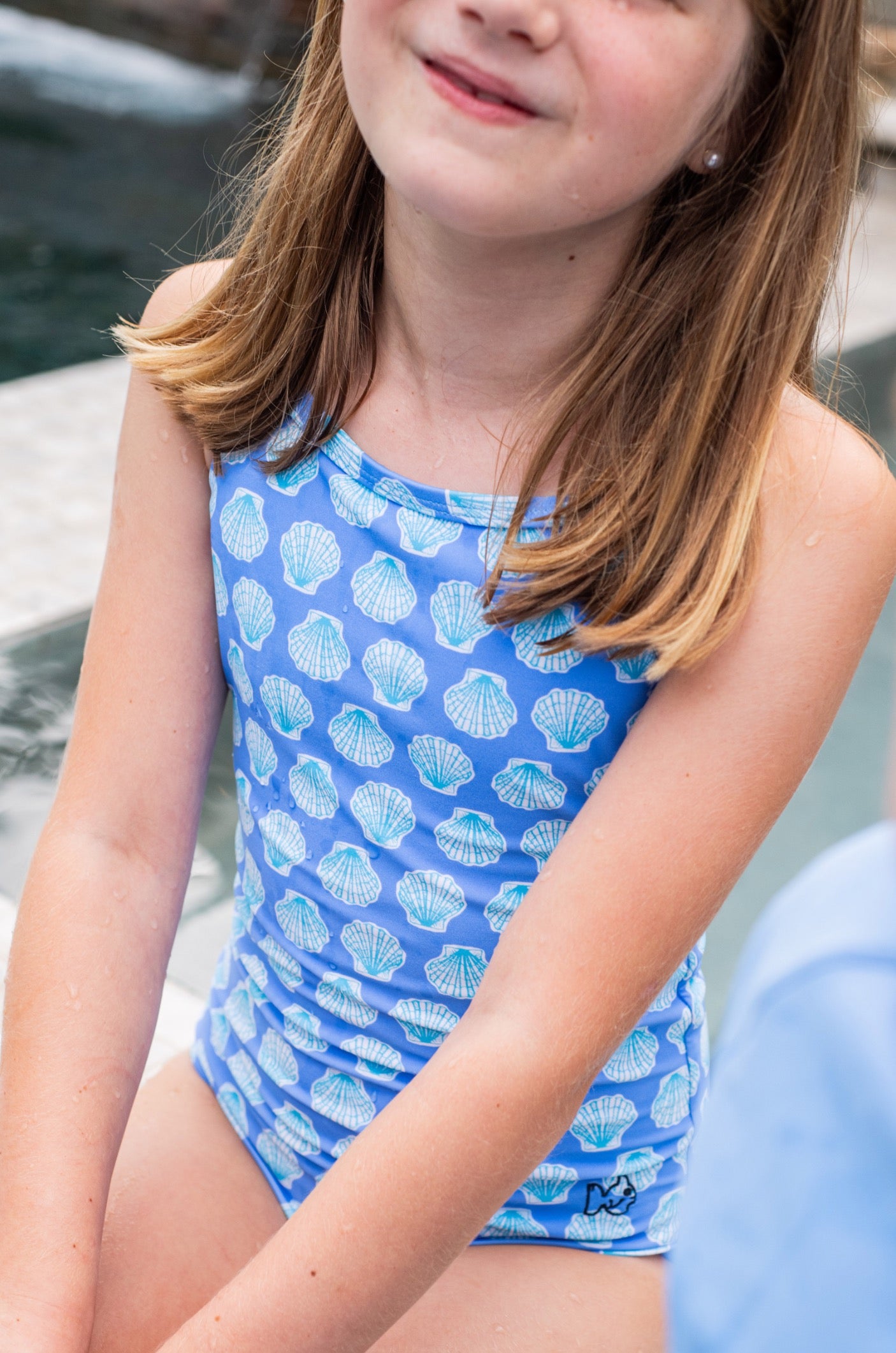 Child wearing a blue swimsuit with shell pattern by a pool