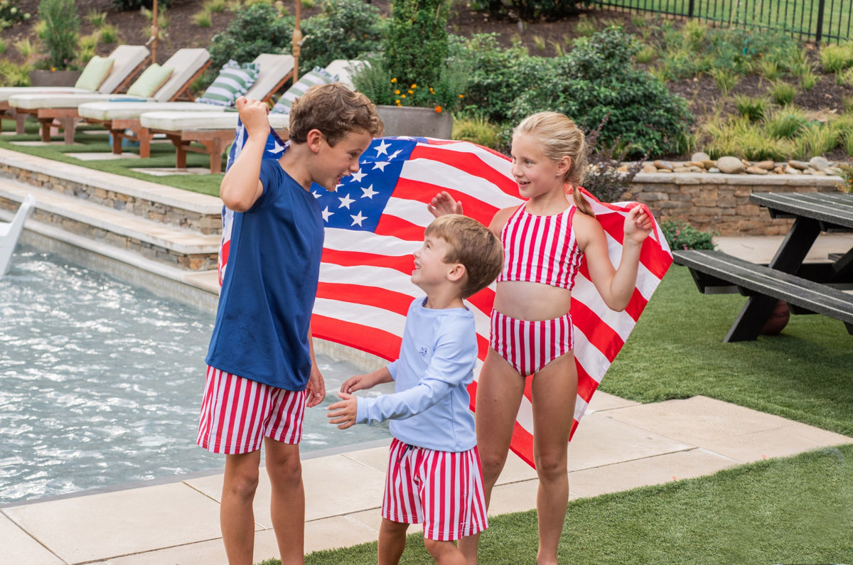 Three children holding an American flag by a poolside.
