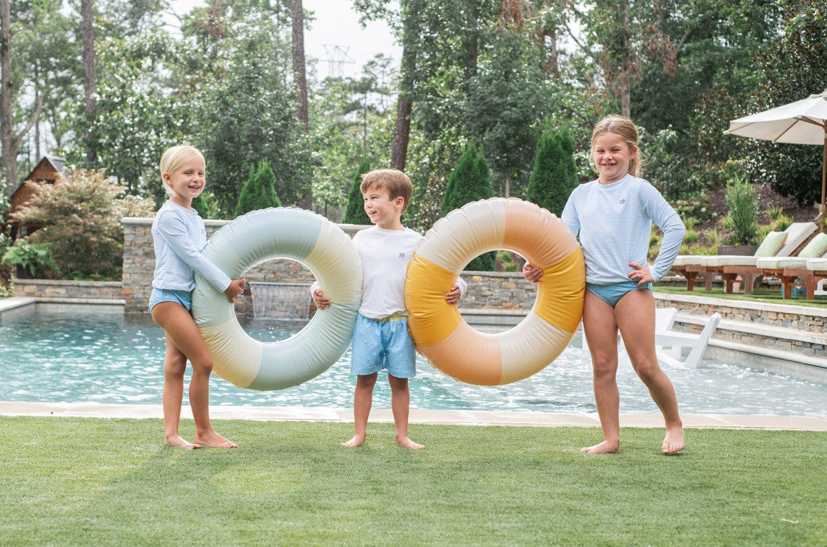 Three children holding colorful inner tubes by a pool
