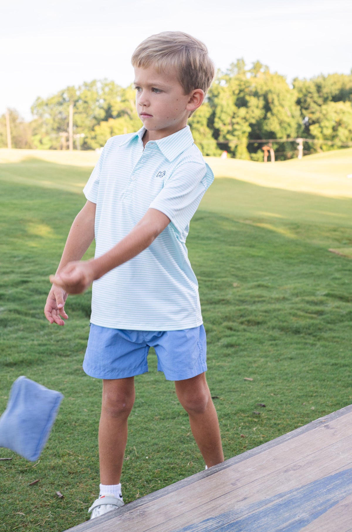 Young boy wearing a light blue polo playing on a grassy field