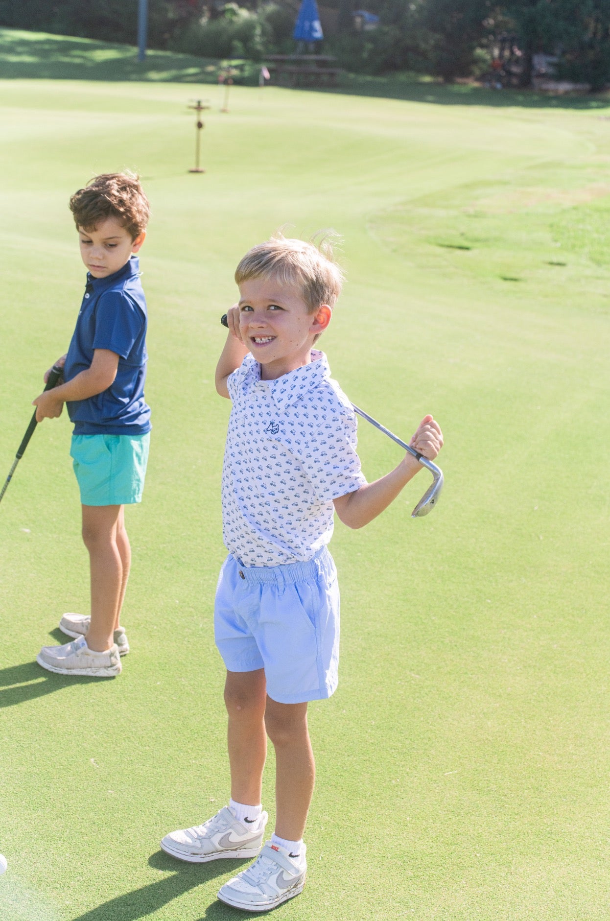 Two young boys wearing golf patterned performance polos and playing golf on a golf course
