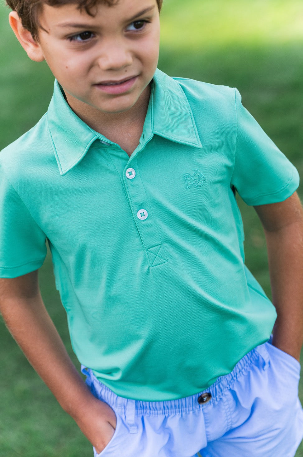 Young boy wearing a teal polo shirt and light blue shorts standing outdoors.