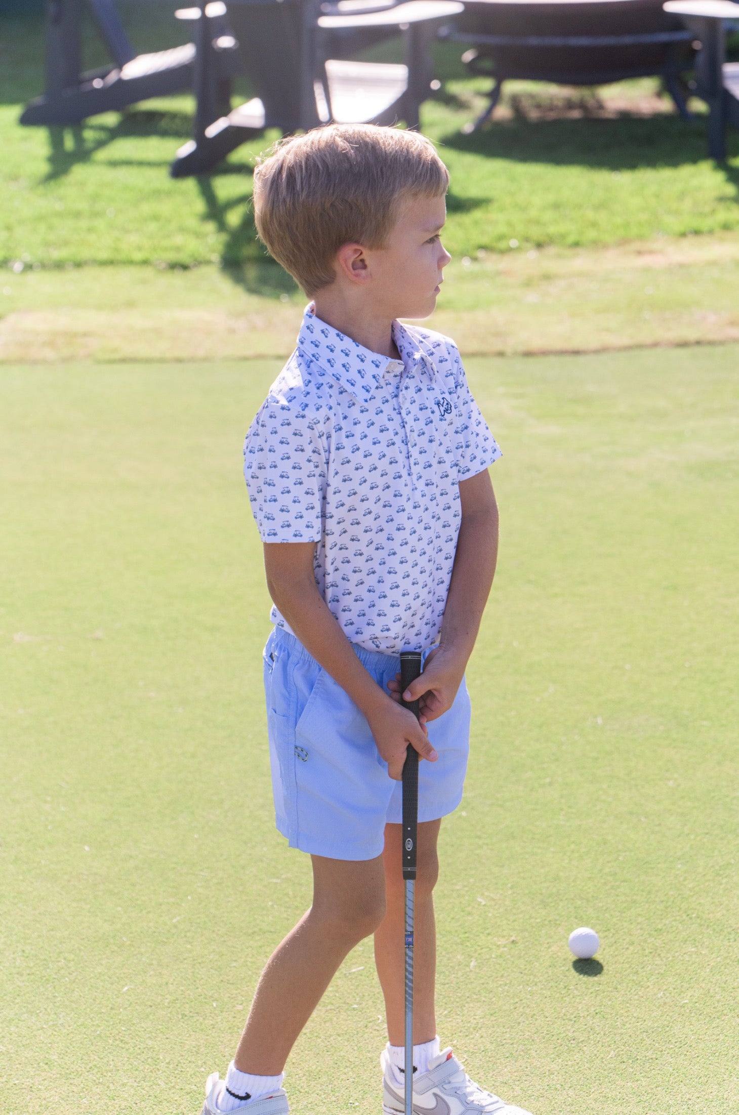 Young boy on a golf course holding a putter and ball
