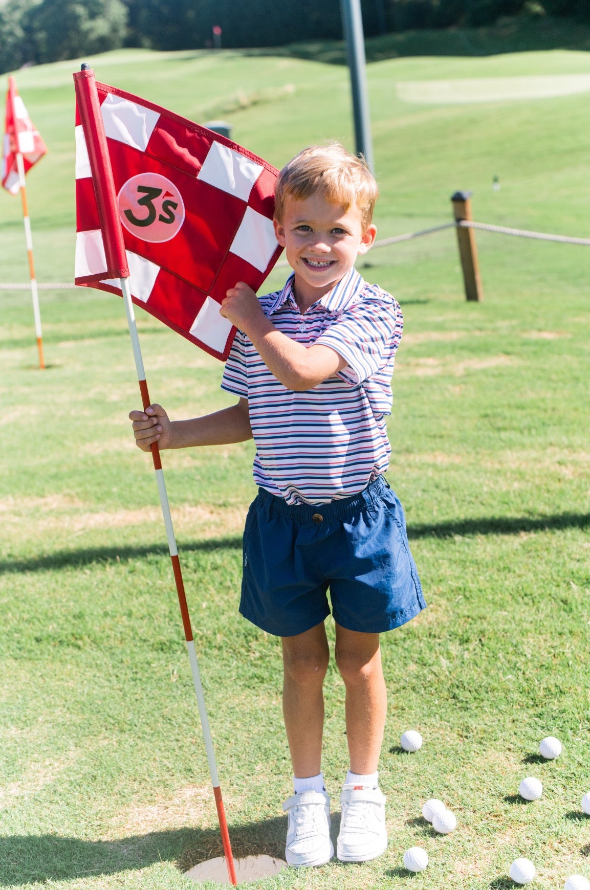 Child holding a golf flag on a golf course wearing performance polo for kids