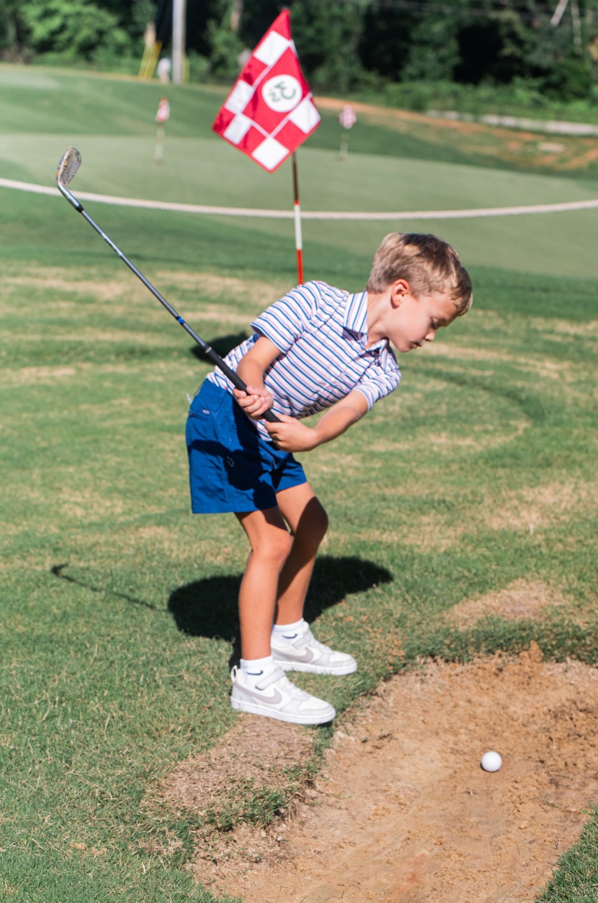Child playing golf on a green course wearing patriotic striped polo shirt