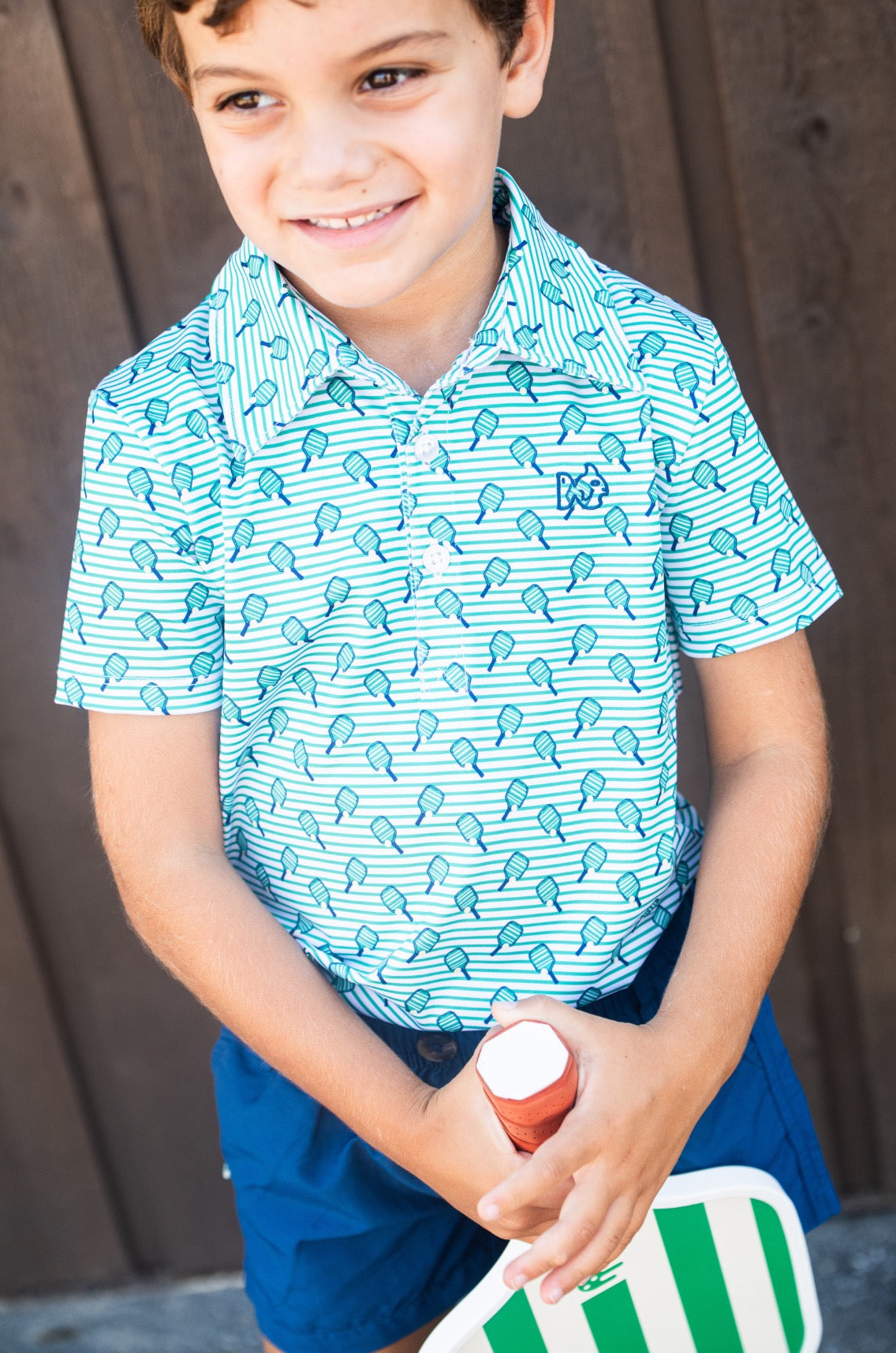 Child wearing a blue patterned shirt holding a sports ball against a wooden background