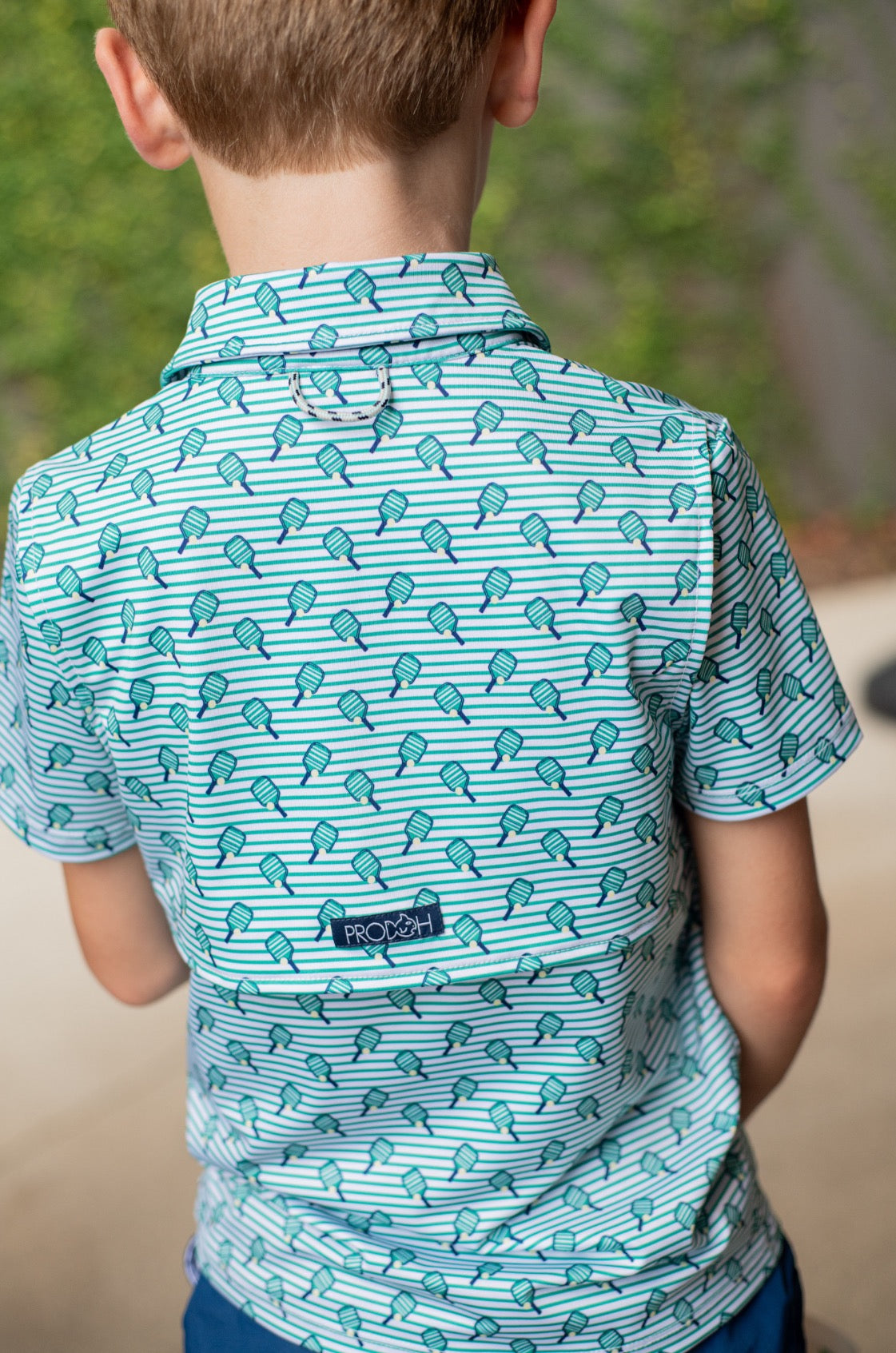 Child wearing a blue patterned shirt with a small prodoh brand logo on back.