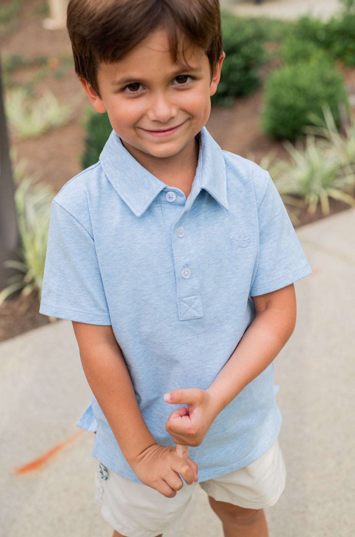 Young boy wearing a light blue polo shirt and white shorts outdoors.