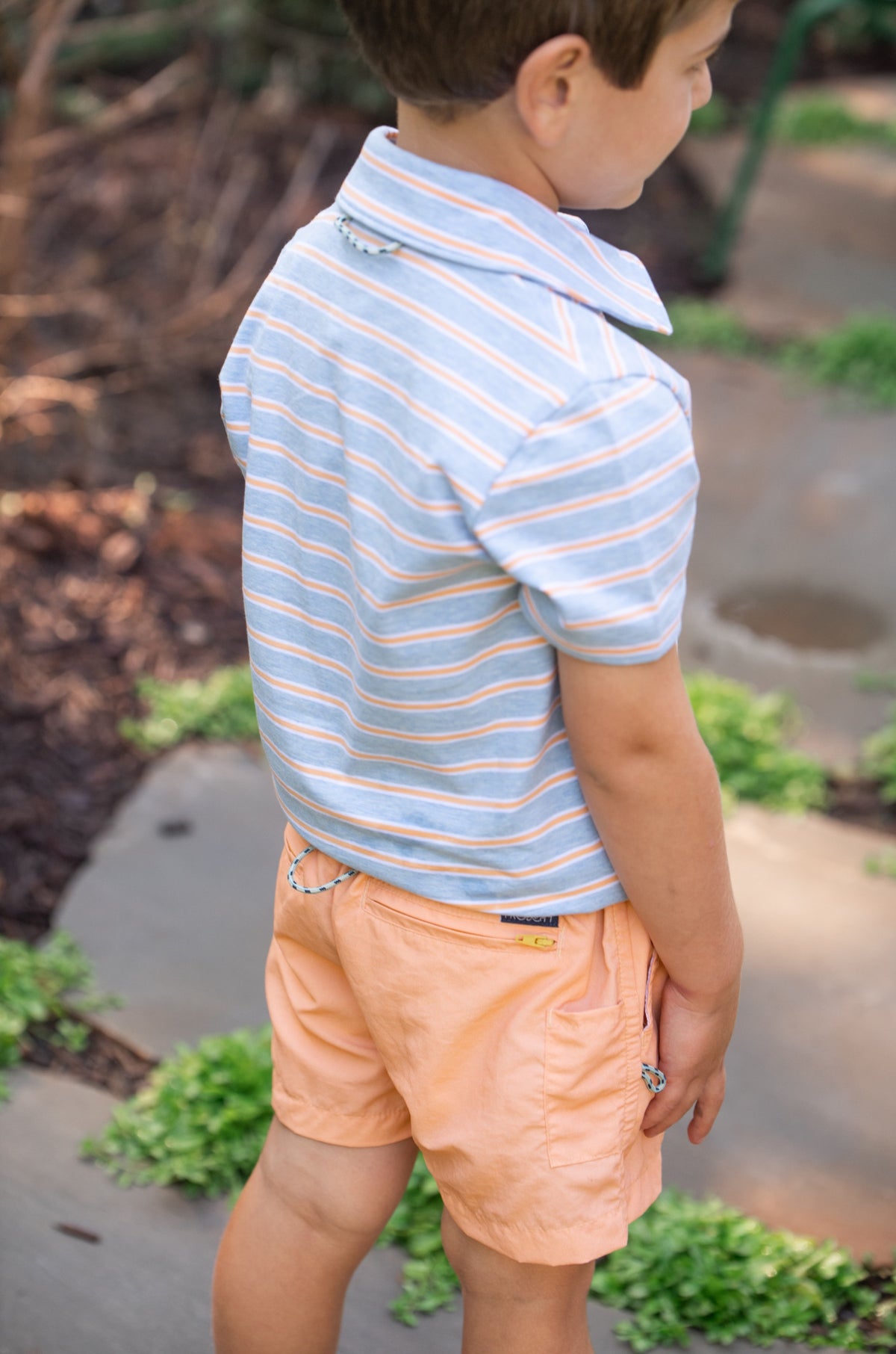 Child wearing a orange striped cotton polo shirt and orange shorts outdoors