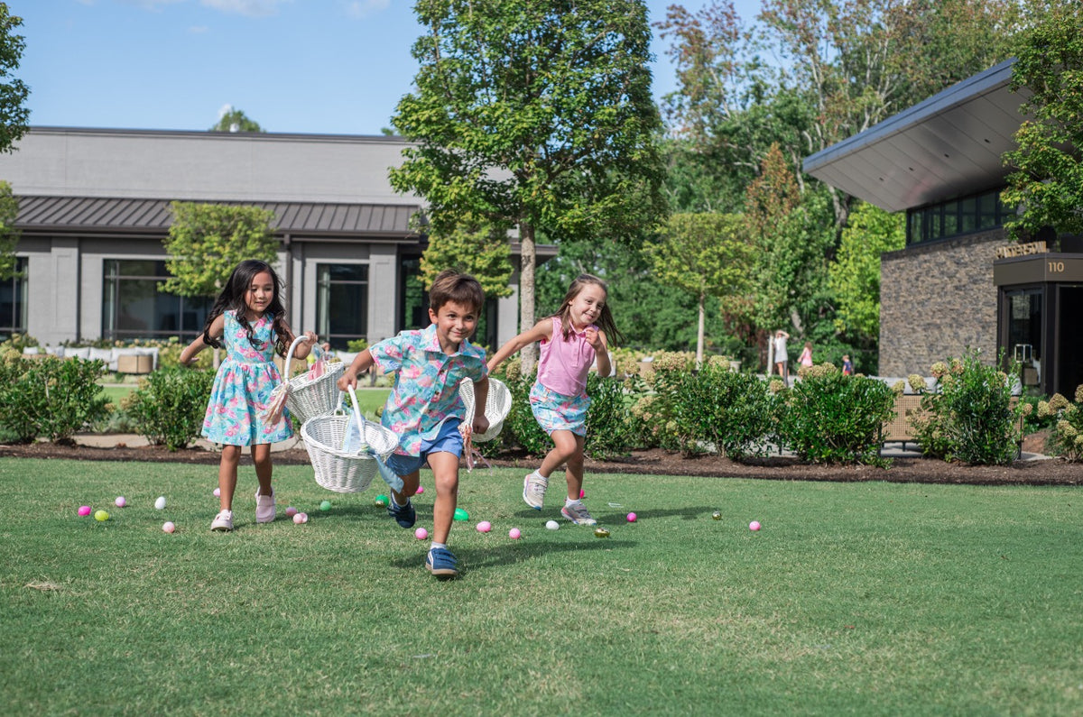 Three children playing with Easter baskets in a garden with floral pattern shirts