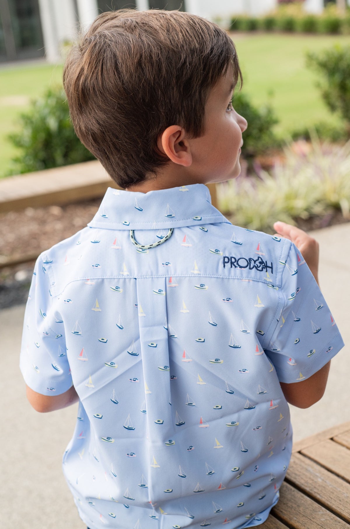 Child wearing a light blue shirt with sailboat pattern outdoors
