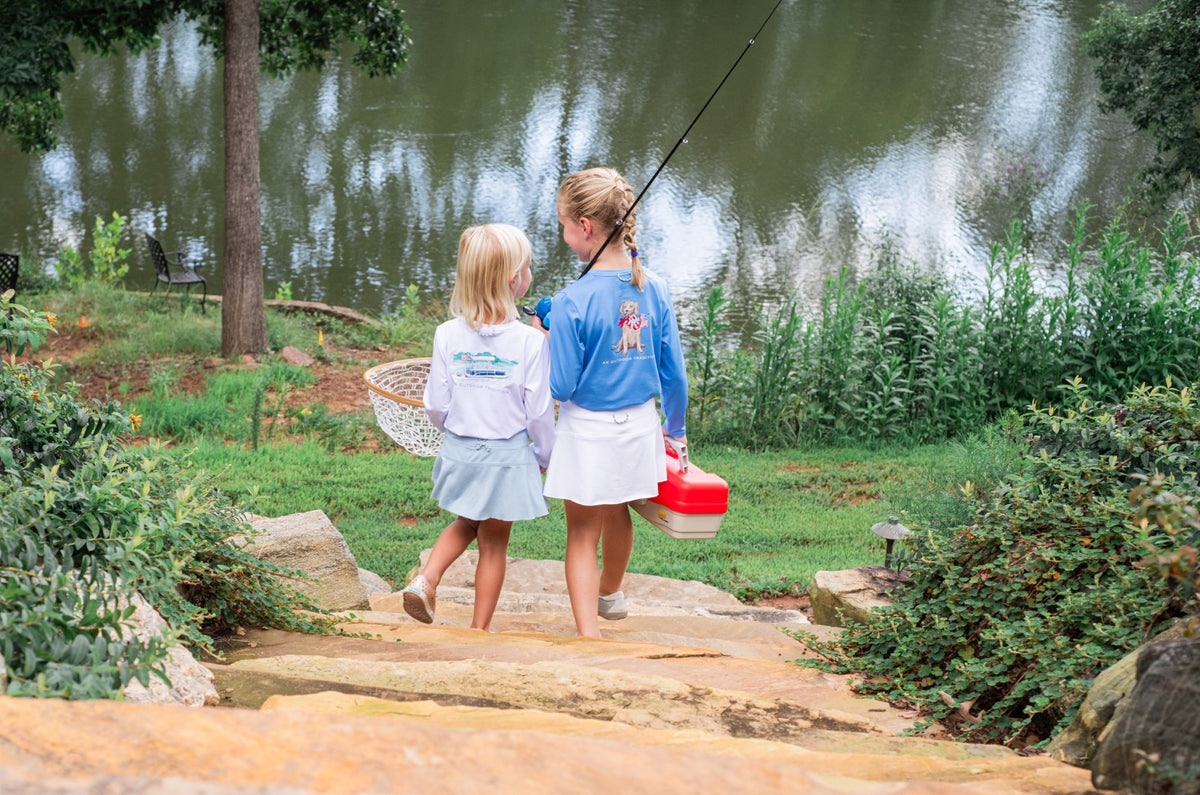 Two young girls walking by a lake with fishing gear wearing their long sleeve performance shirts