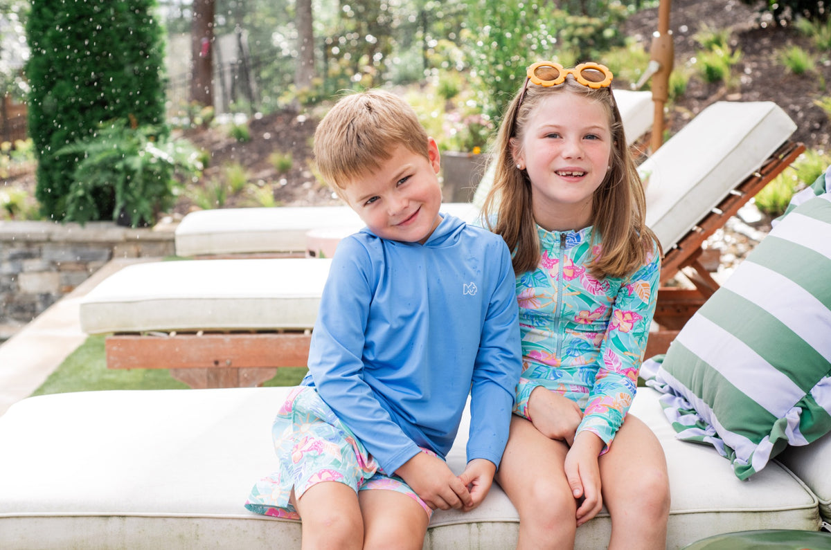 Two children sitting on a patio chair outdoors wearing blue hoodie
