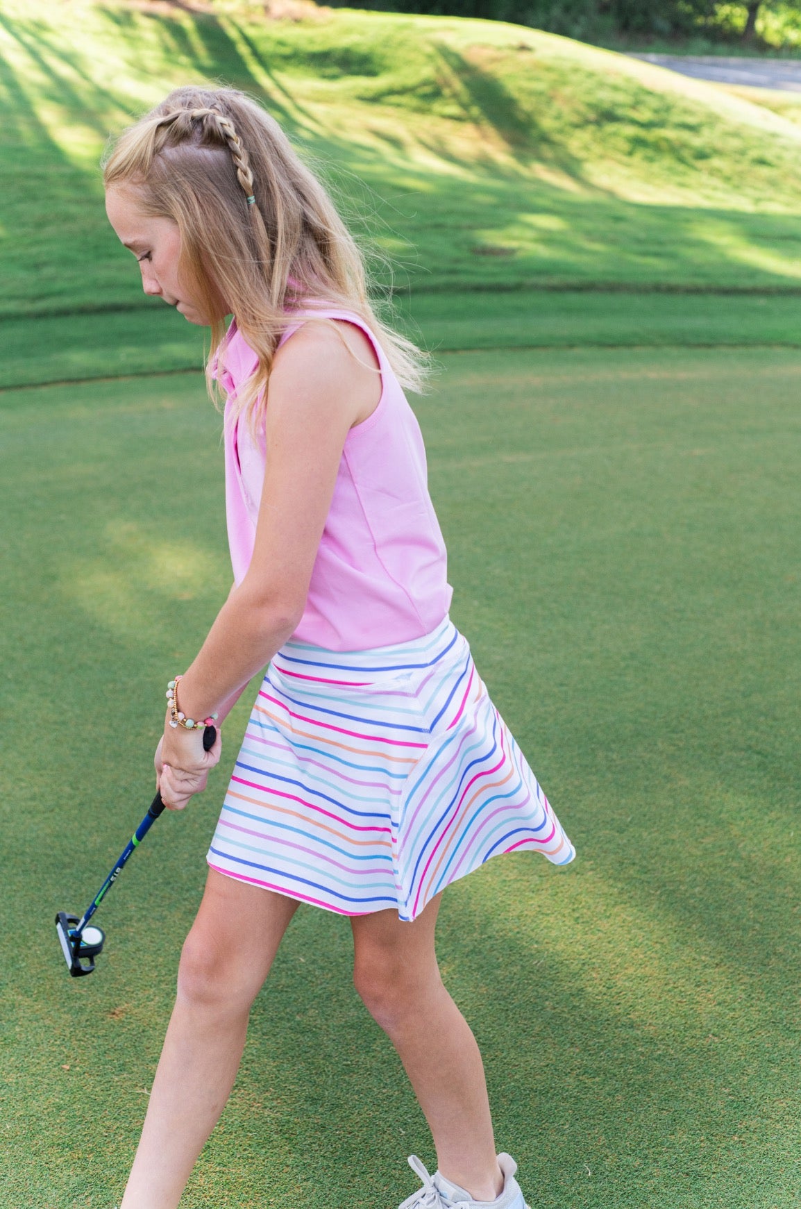 Young girl playing golf on a green course with sleeveless polo shirt