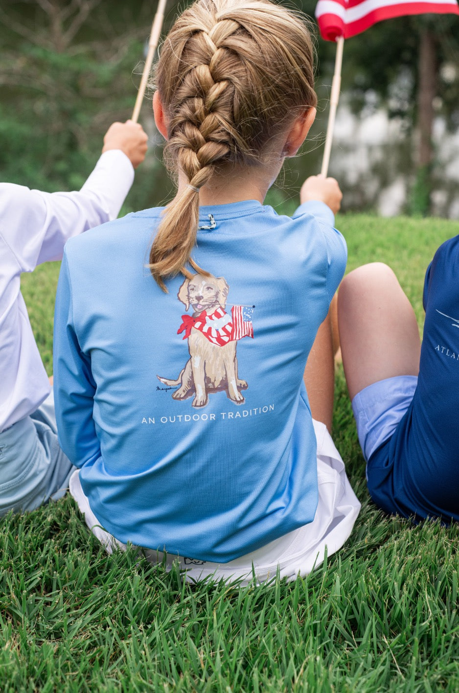 Child wearing a blue shirt with a dog graphic sitting on grass