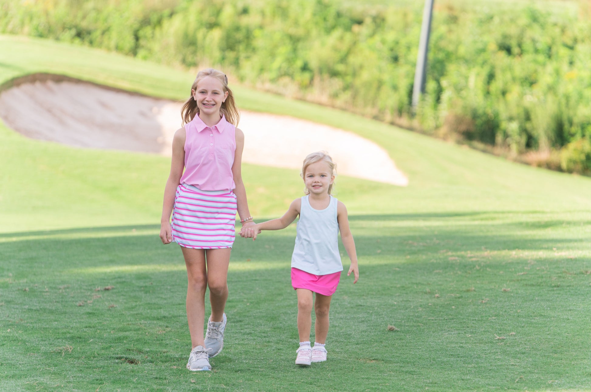 Two young girls holding hands on a golf course wearing polo shirts