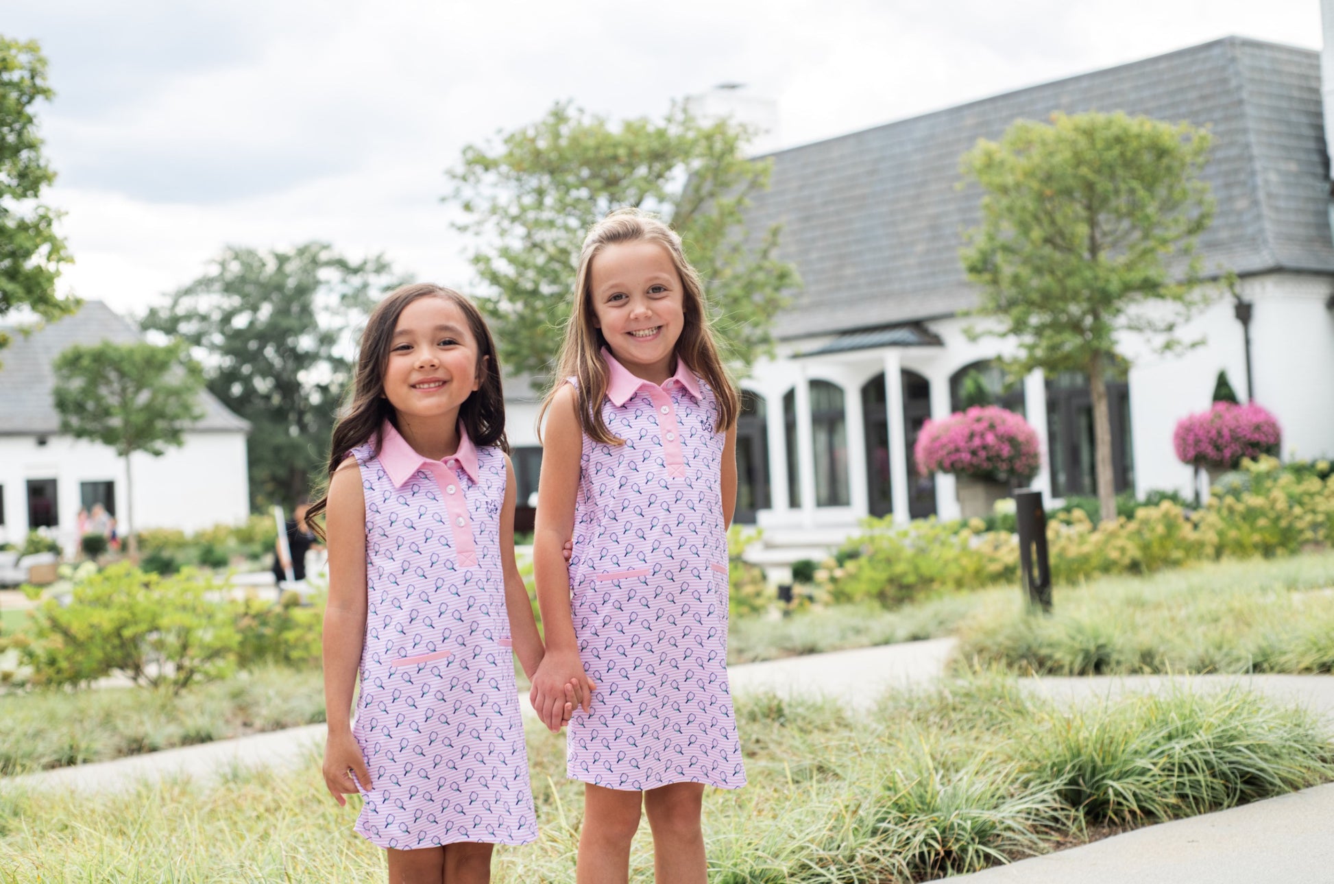 Two young girls in matching pink sleeveless polo dresses standing in a garden