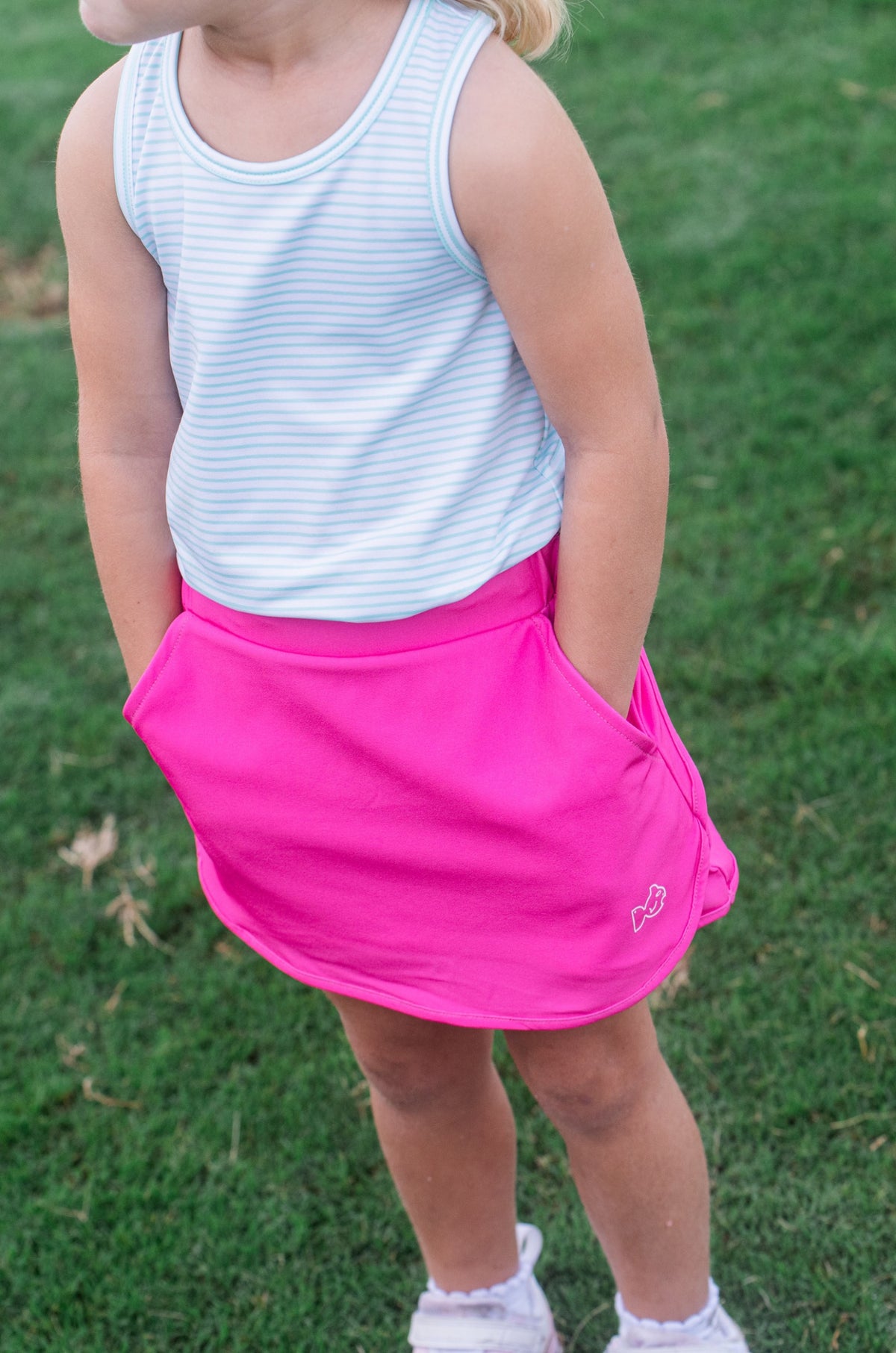 Child wearing a pink skirt and white striped tank top on grass