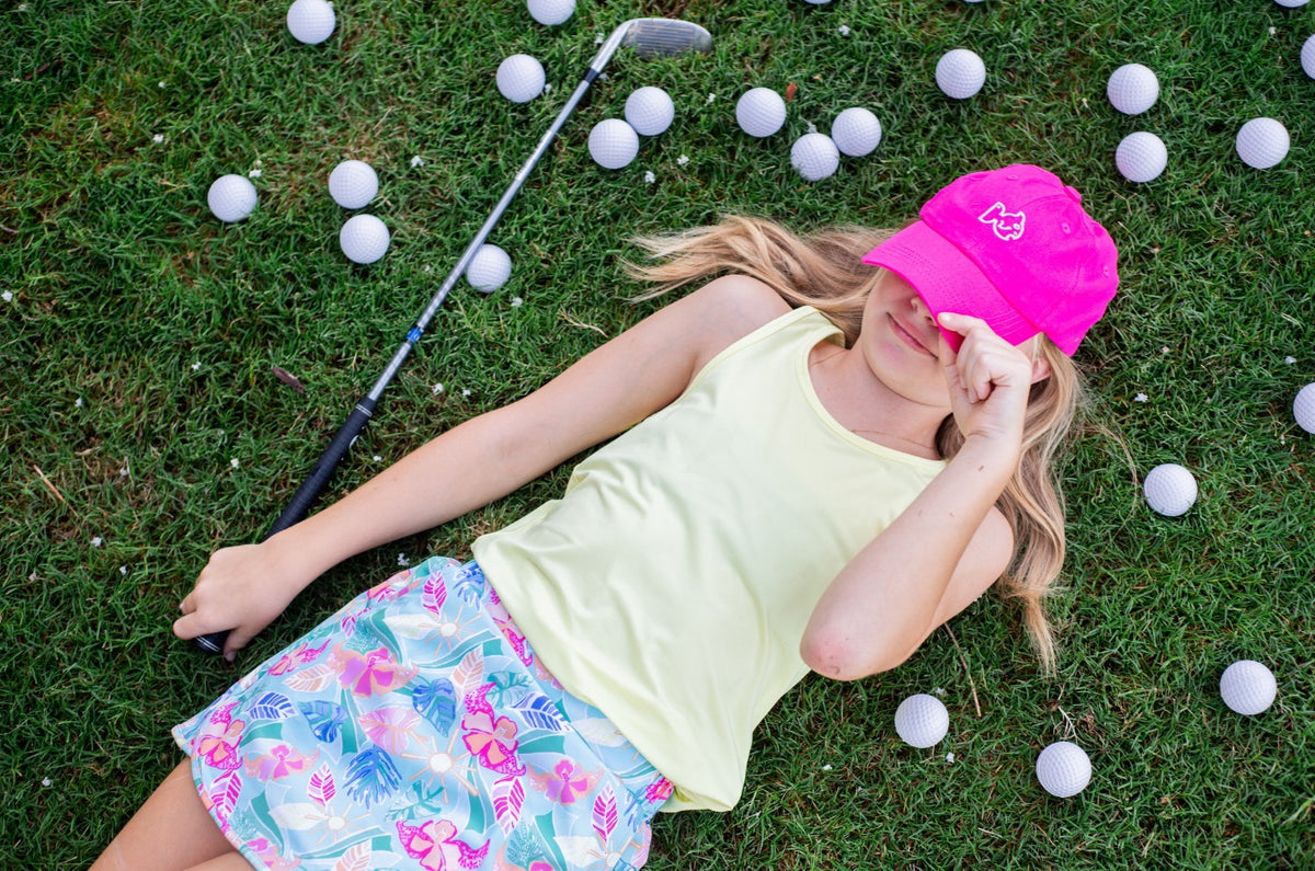 Young girl wearing quick-dry performance tank top while lying on grass with golf equipment and balls