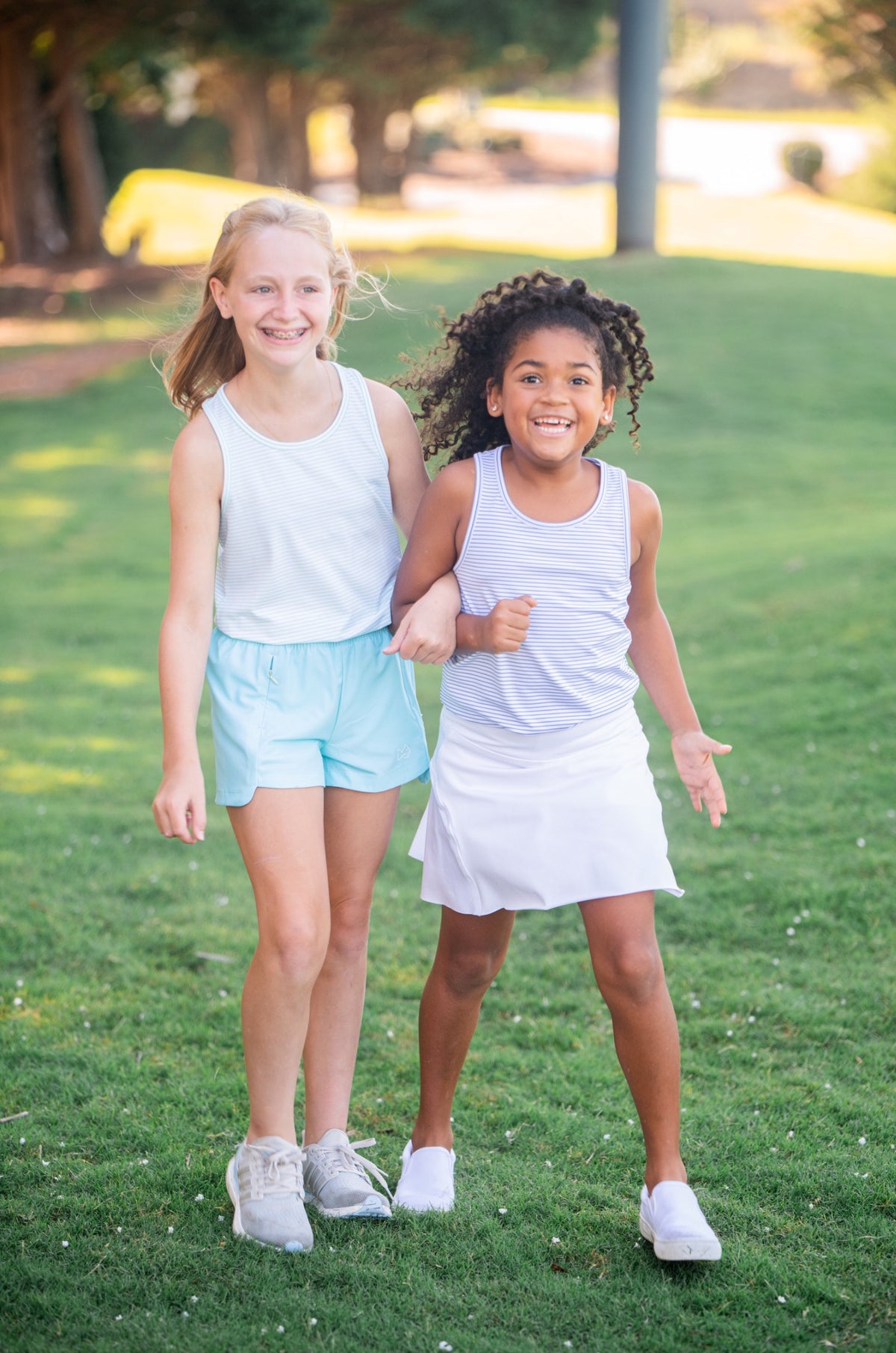 Two young girls wearing performance tank-tops standing on grass
