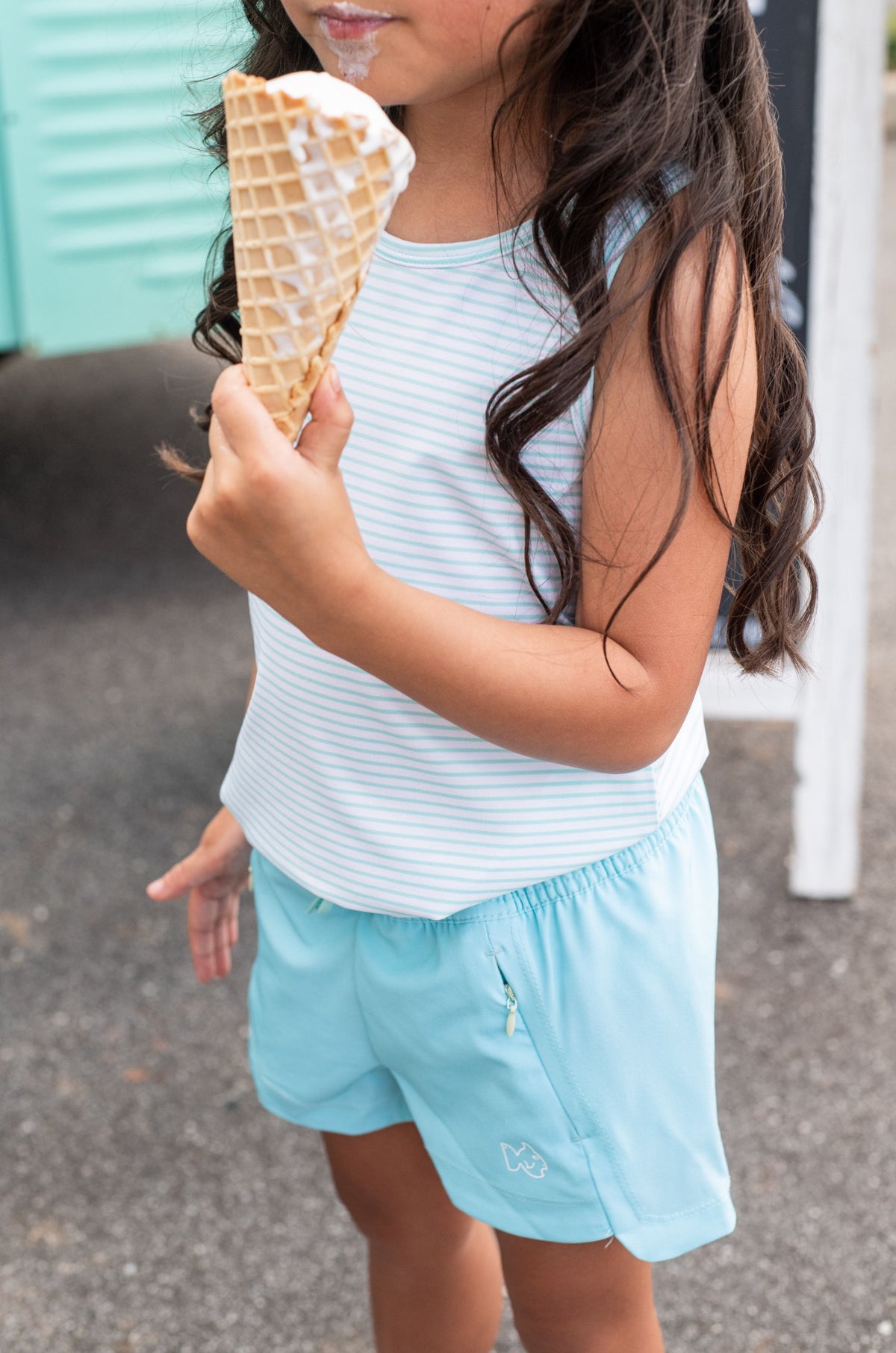 Child holding an ice cream cone wearing a light blue sleeveless top and quick-dry shorts.
