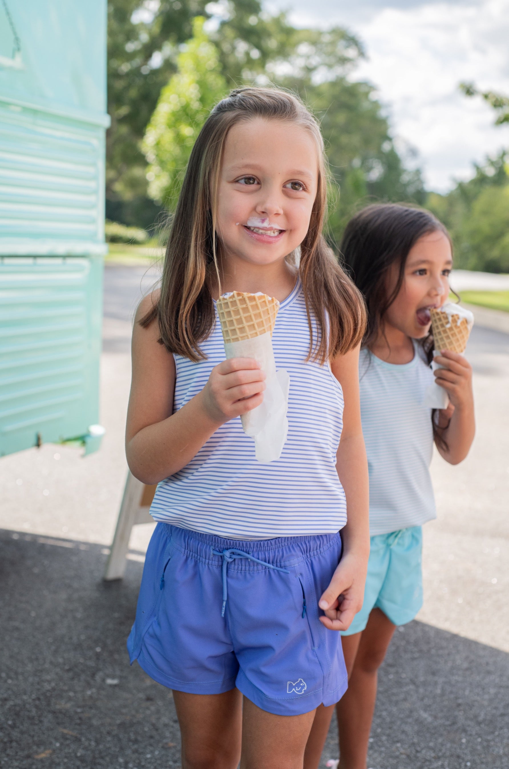 Two young girls enjoying ice cream cones wearing purple beach cruiser shorts