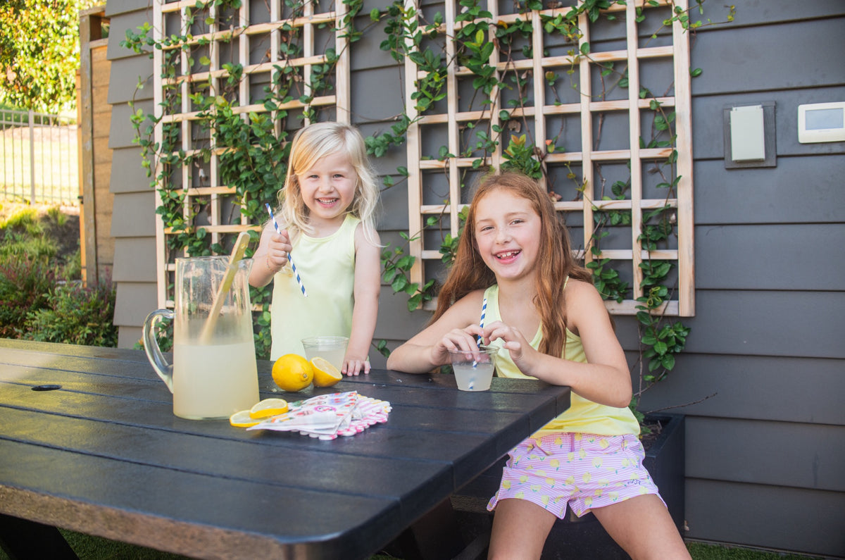 Two young girls wearing performance shorts at a table outdoors drinking lemonade