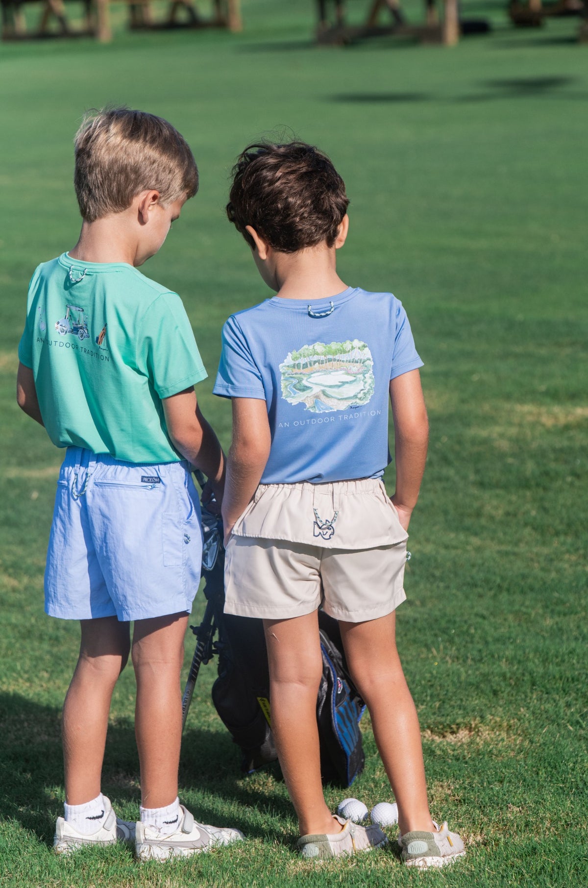 Two children standing on a grassy field wearing matching performance t-shirts and shorts