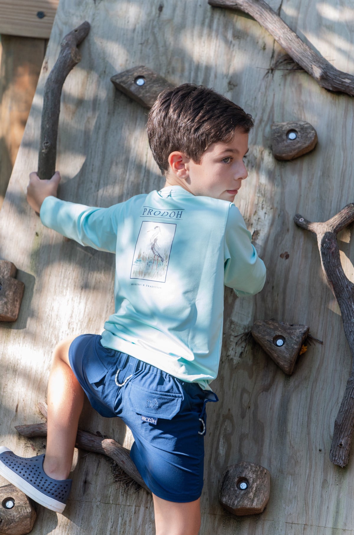 Child climbing a wooden climbing wall with a light blue quick-dry long Sleeve T-shirt