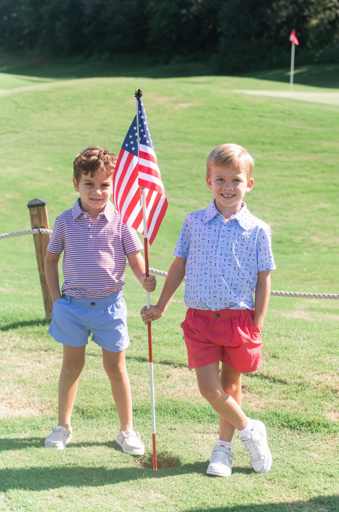 Two young boys holding an American flag on a golf course wearing red shorts