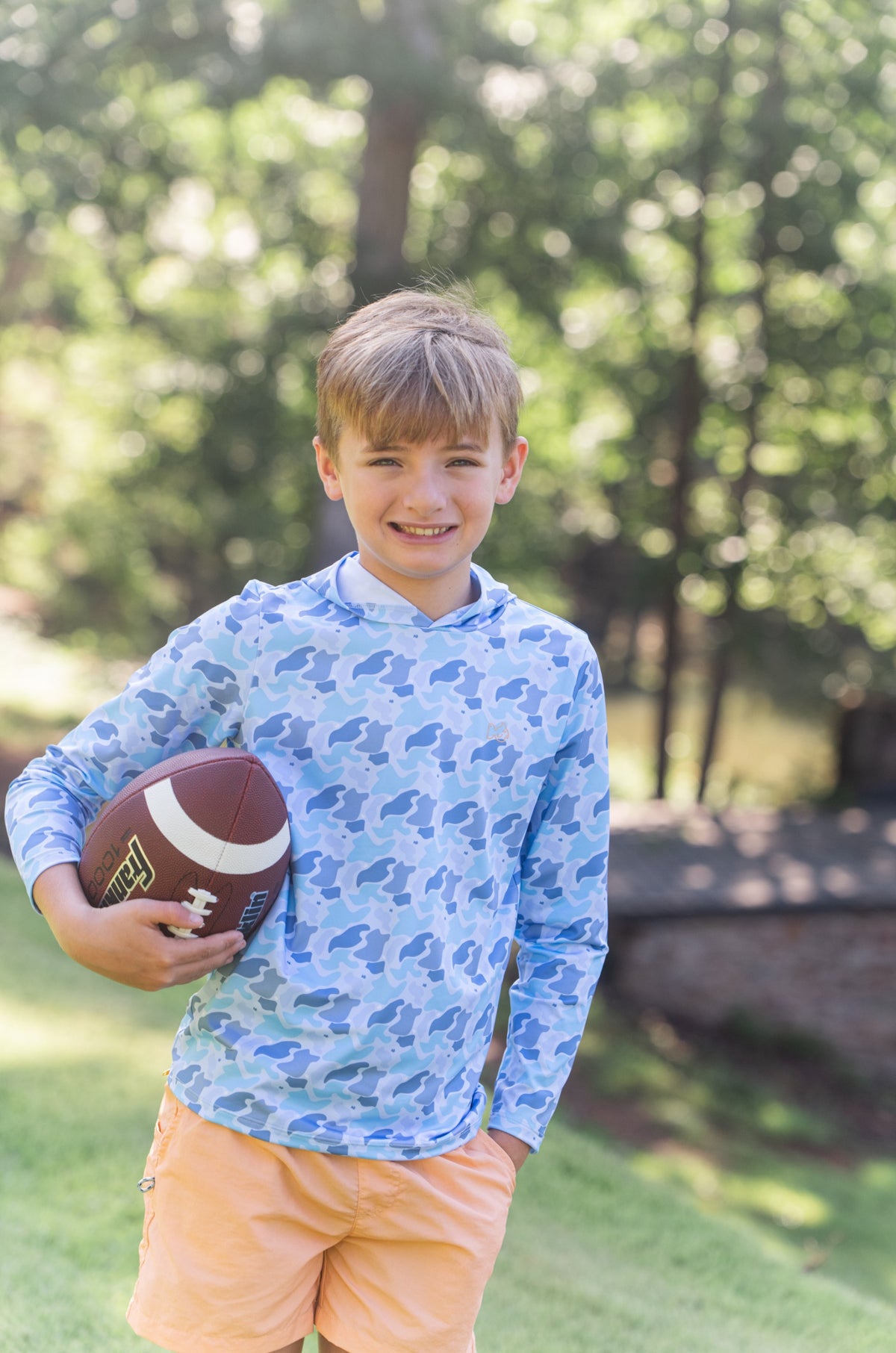 Young boy holding a football wearing orange performance Shorts