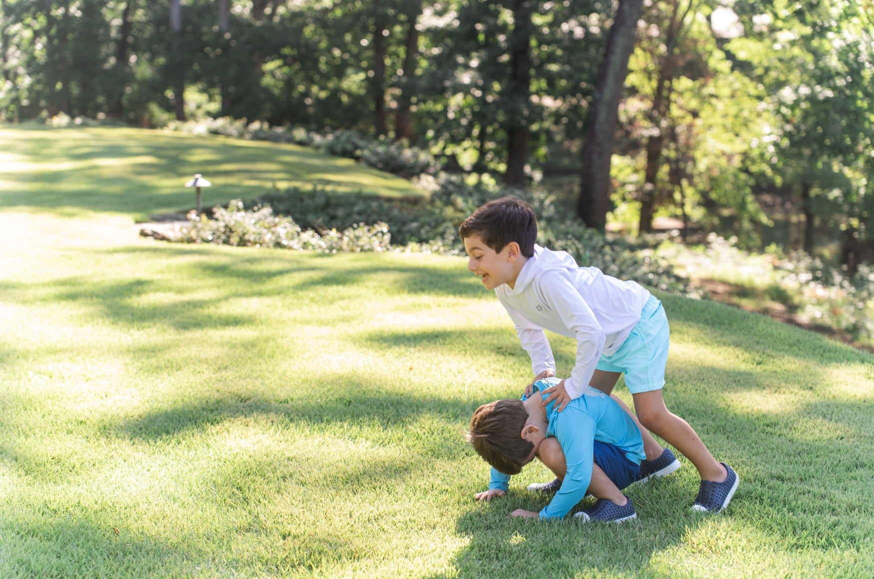 Two children playing on a grassy lawn with trees in the background