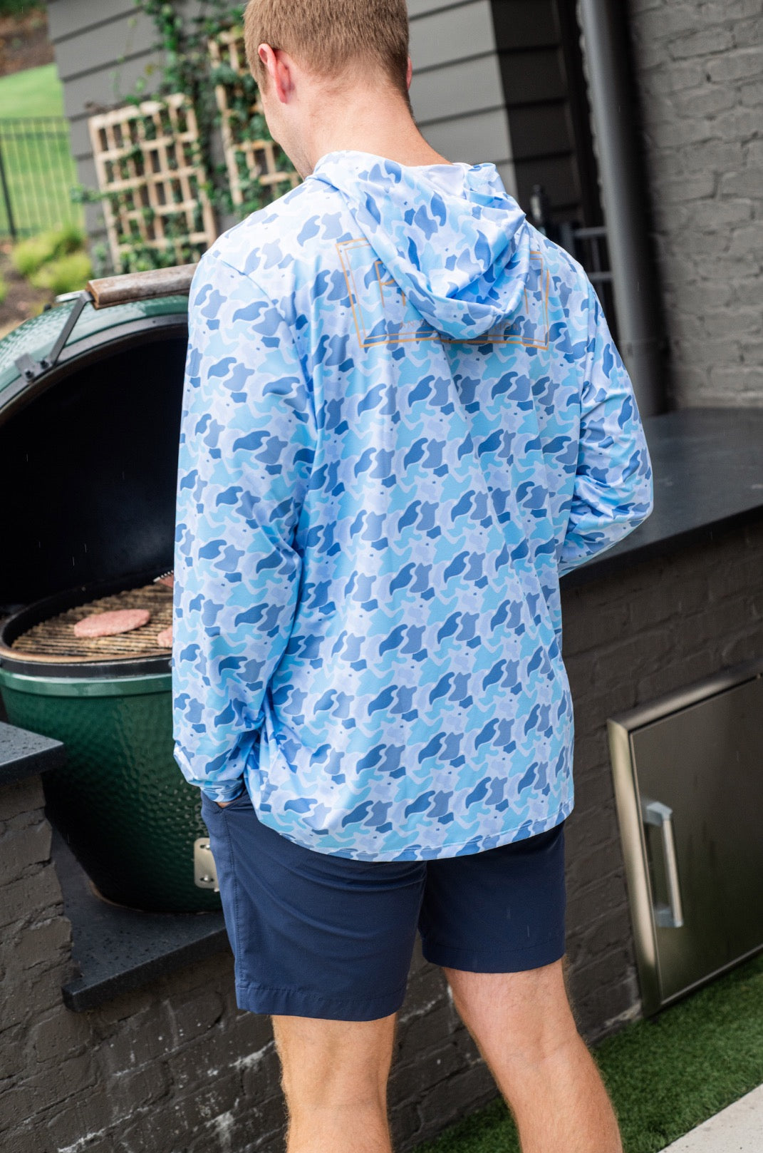 adult man wearing a blue patterned hoodie standing outdoors near a grill.