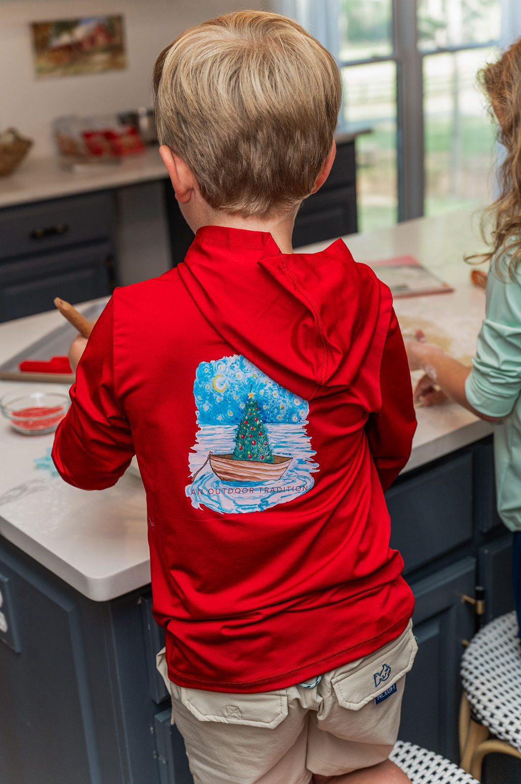 Child wearing a red hoodie with a Christmas design in a kitchen