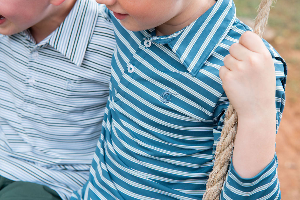A close-up of a child wearing a blue and white striped long-sleeve polo shirt while sitting on a rope swing outdoors.