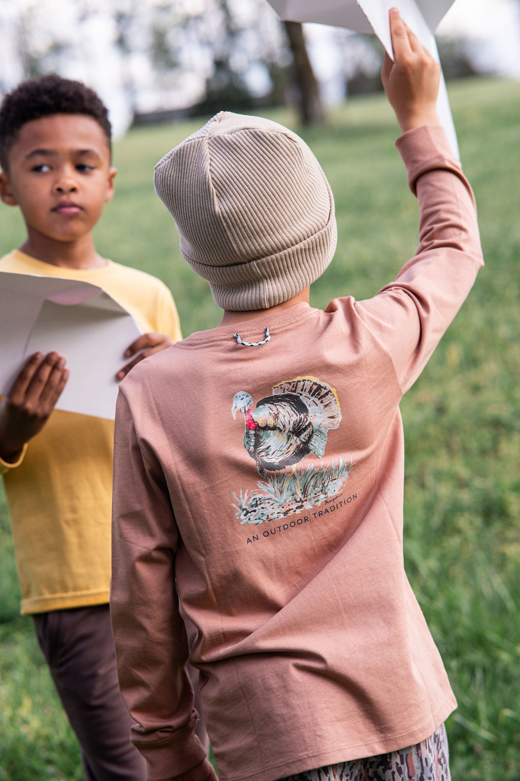 young boy wearing a brown sweatshirt with a graphic turkey design playing outdoors